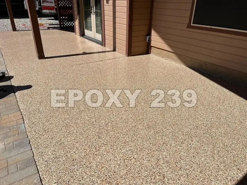 Back patio in warm Creekbed flake epoxy beside a wood-sided house